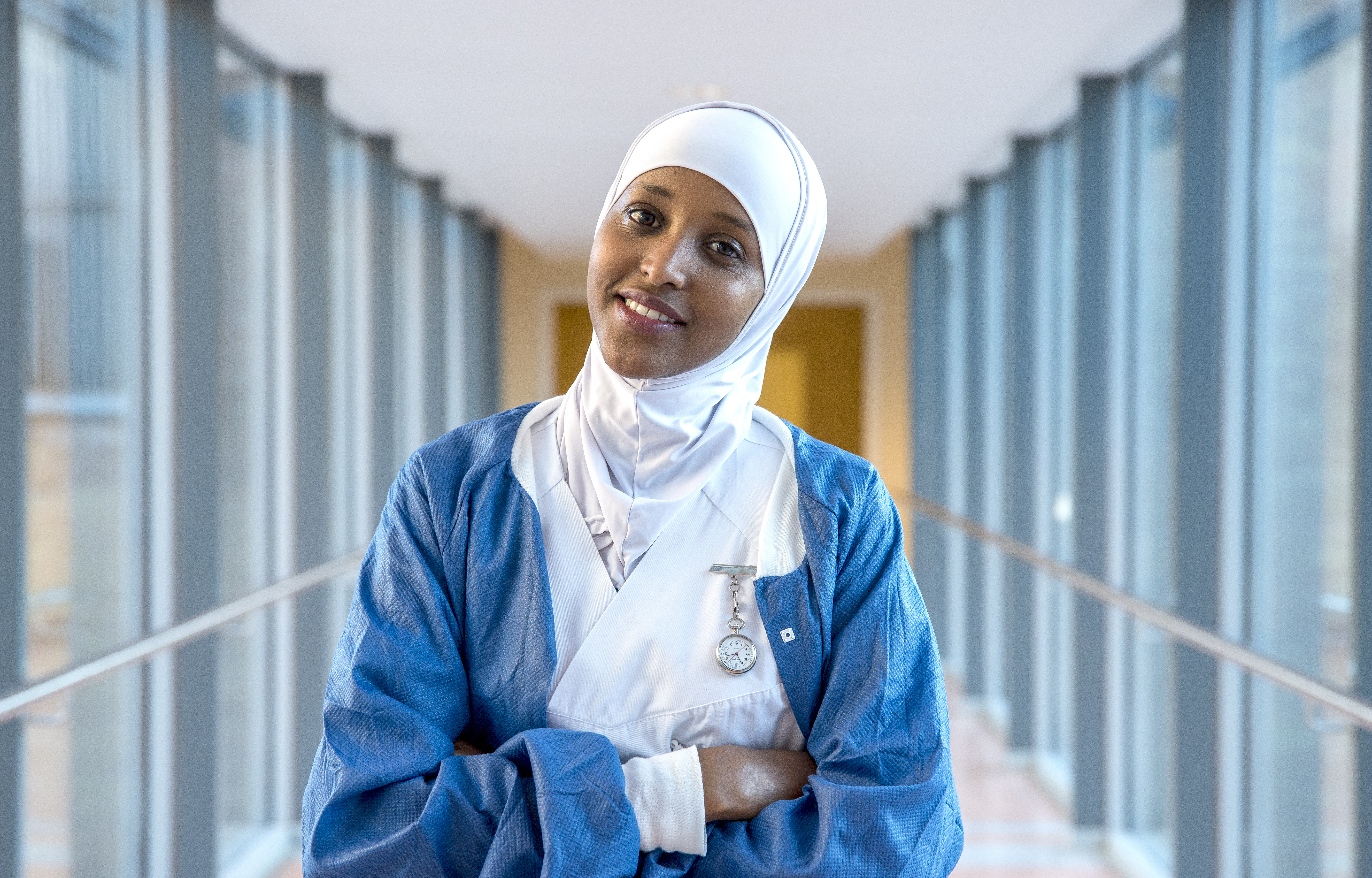 Bilde av en blid mørkhudet medarbeider i sykehusuniform med hitshab 