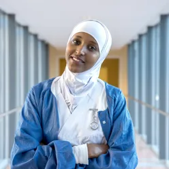 Bilde av en blid mørkhudet medarbeider i sykehusuniform med hitshab