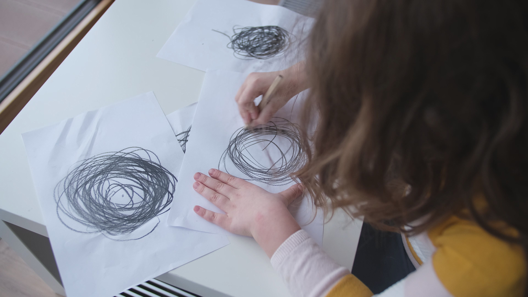 Bakhodet til jente med brunt hår tegner sorte kruseduller på hvitt ark