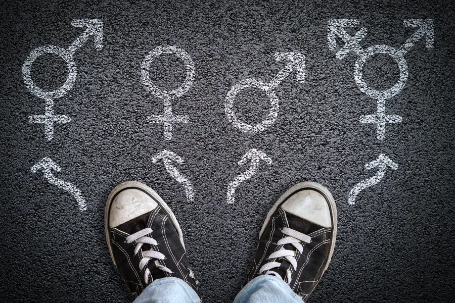 To sko som står på asfalt. Foran skoene er det tegnet ulike kjønnstegn.