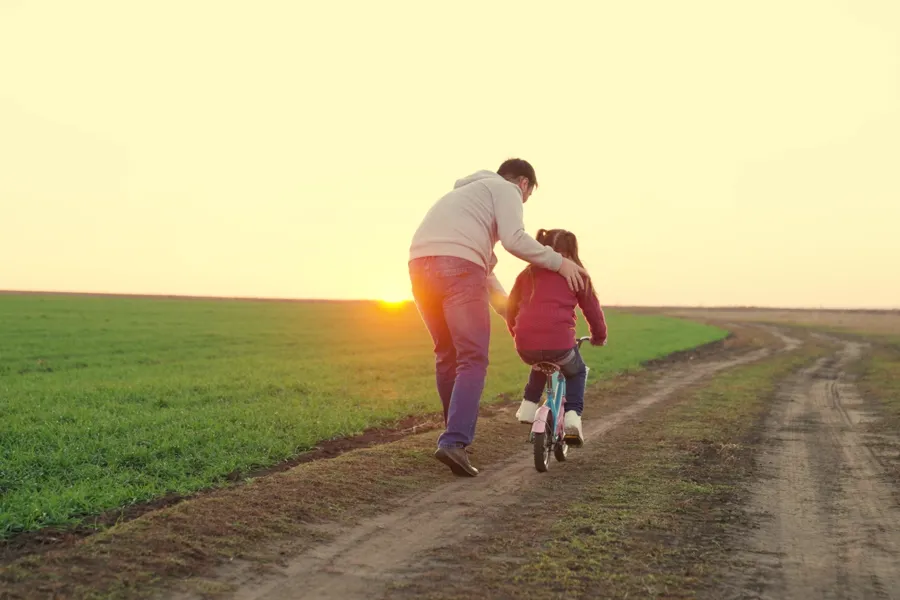 barn på sykkel som støttes av forelder