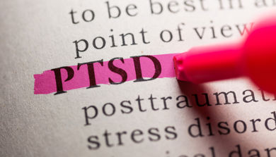 Hånd med merkepenn streker ut forkortelsen PTSD i en bok