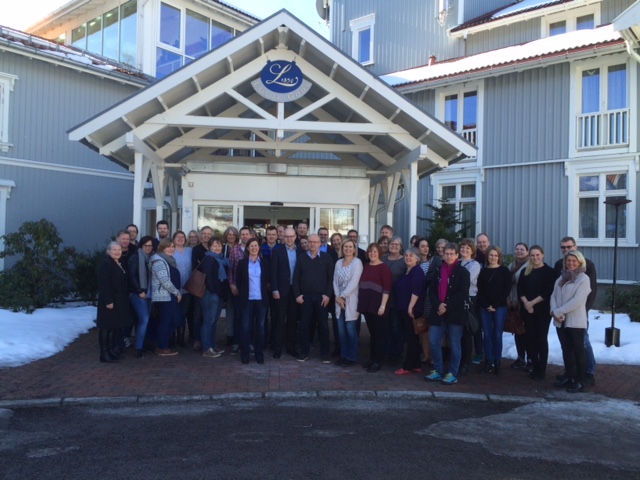 Mange mennesker står foran inngangen til et hus. De smiler til kameraet.