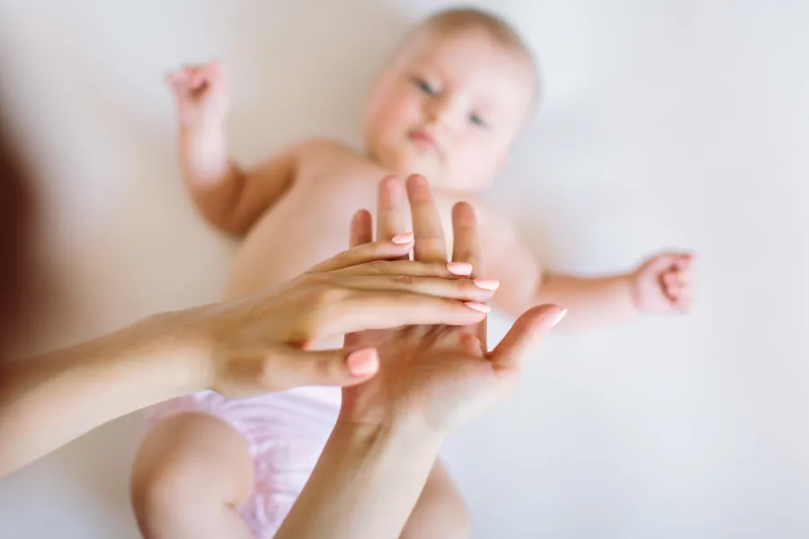 En baby som ligger på en madrass. To voksne hender er i luften over.