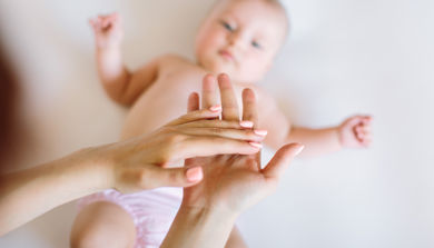 En baby som ligger på en madrass. To voksne hender er i luften over.