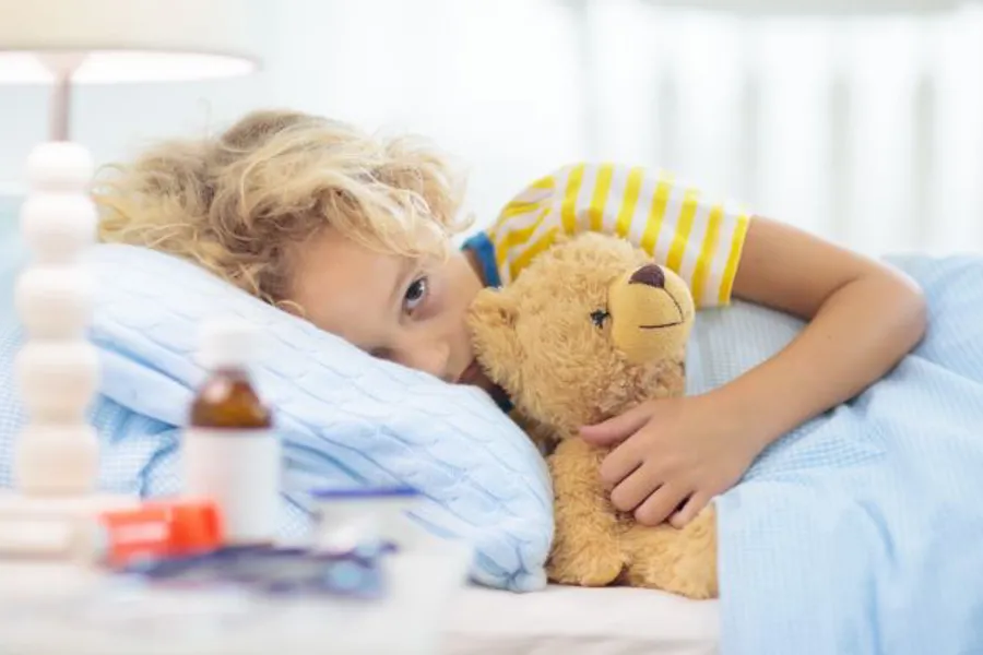 Et barn som ligger i en seng og holder rundt en bamse.