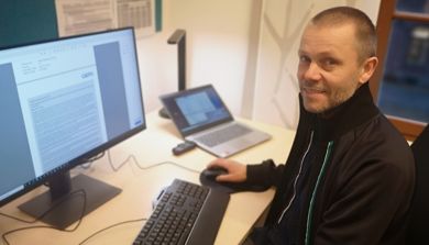 En mann som sitter ved et skrivebord med en datamaskin og en bærbar datamaskin