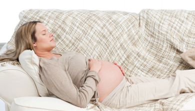 En gravid kvinner ligger på en sofa og holder på magen sin.