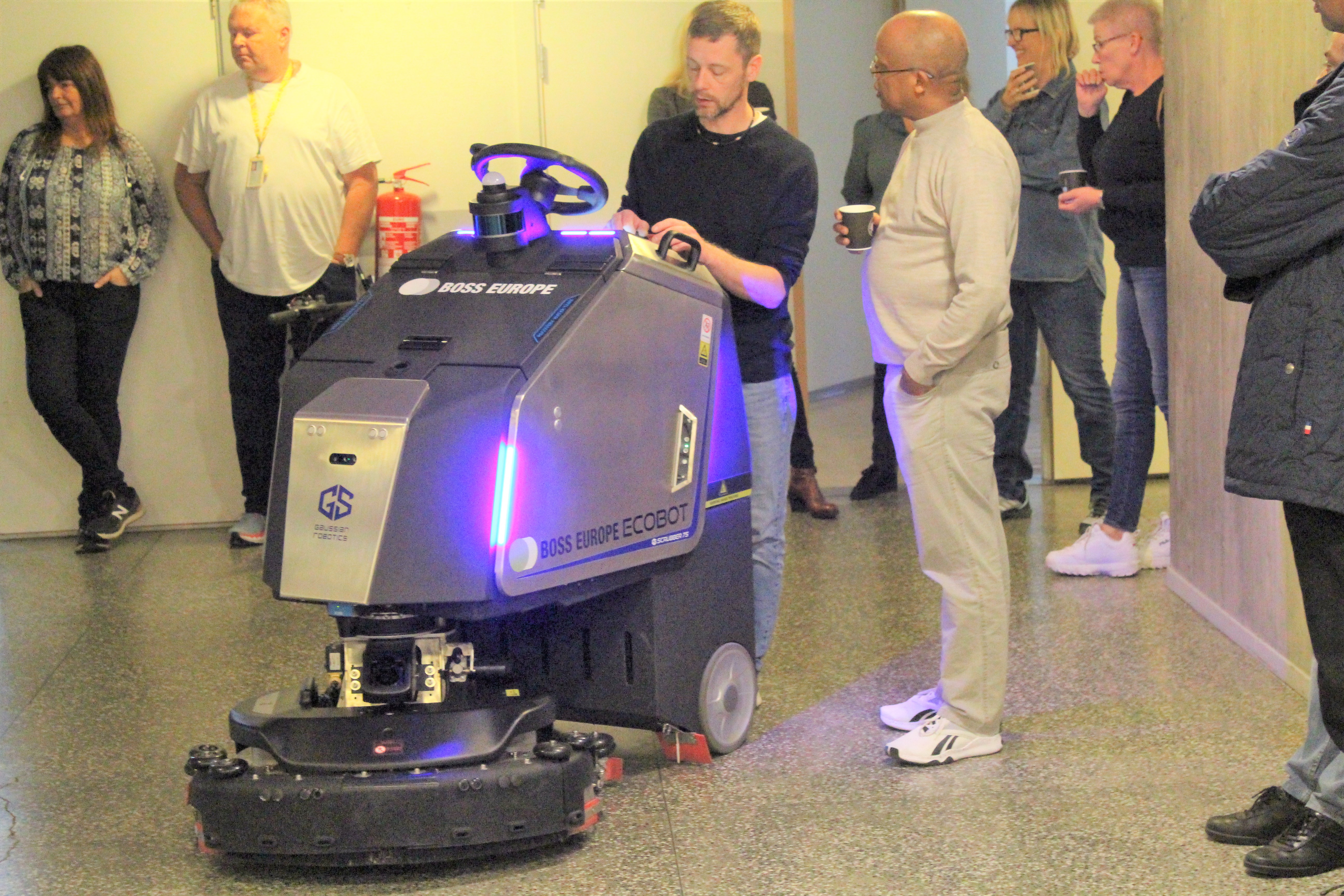 Bildet viser flere personer som står rundt en stor renholdsrobot.