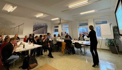 En person som står foran en skjerm og foreleser for flere personer.