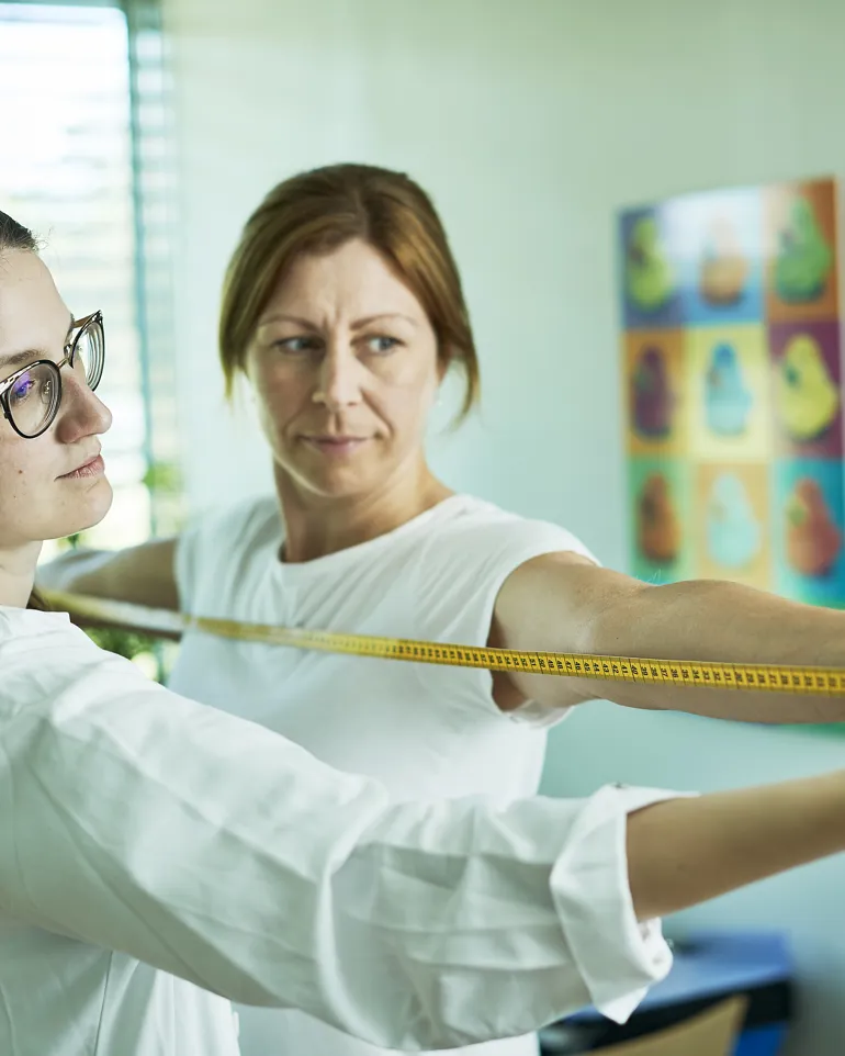 En person som måler en annen person fra fingertupp til fingertupp.