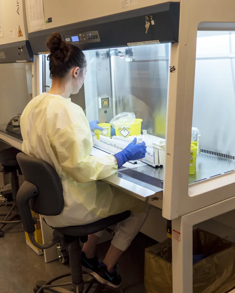 Foto: Bioingeniør som sitter i gul smittefrakk forran et kabinett.