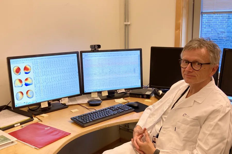 En mann som sitter ved et skrivebord med flere dataskjermer