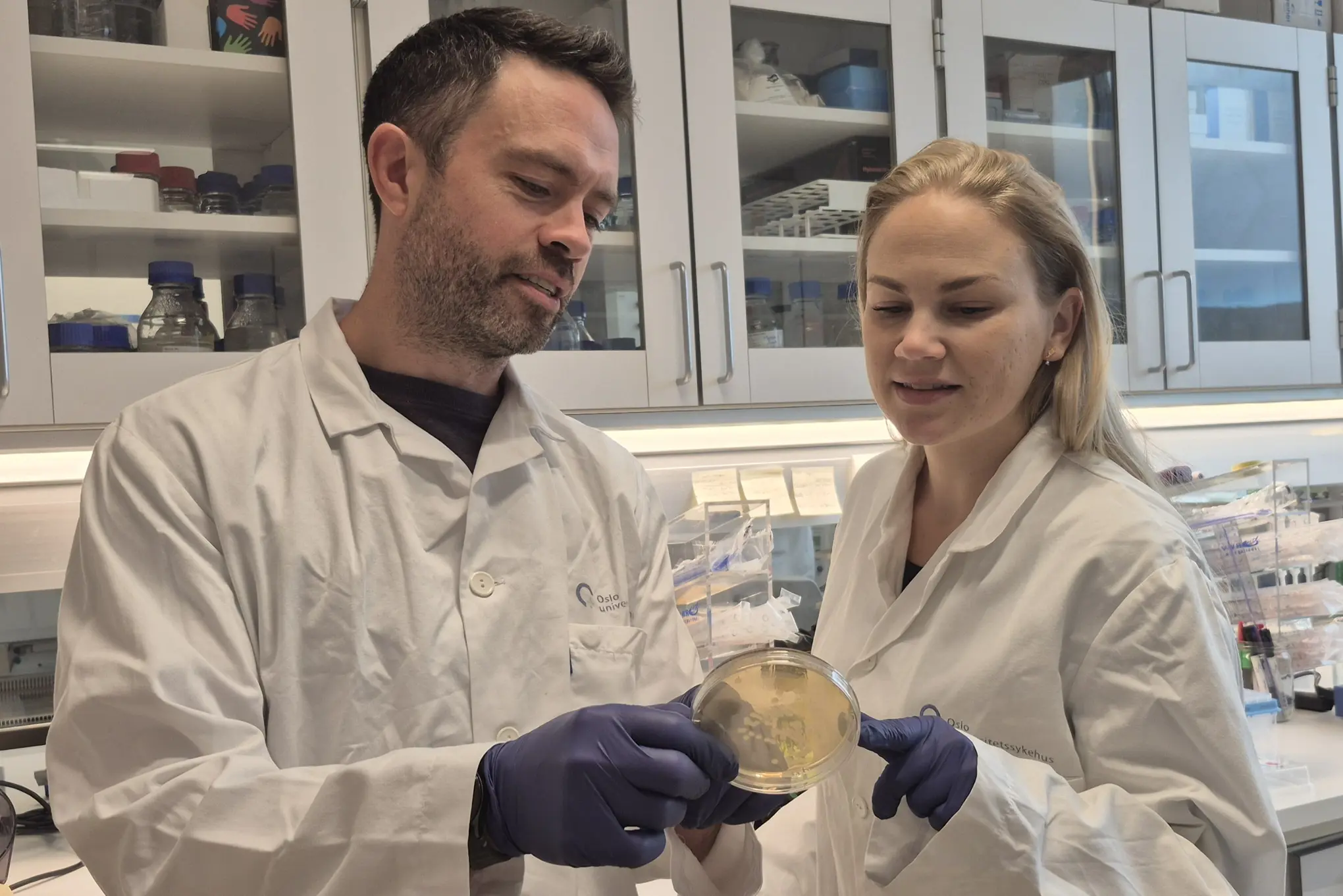 En mann og en kvinne i laboratoriefrakker som ser på et eksemplar