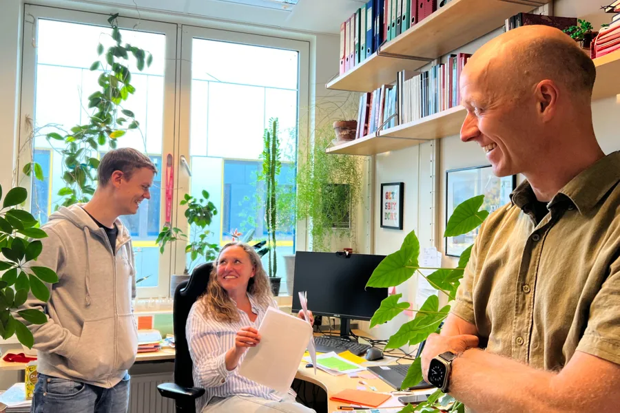 Image showing Andreas Kleppe, Hanne Askautrud and Tarjei Hveem in Hanne's office, when Andreas reveals the good news about funding from the Norwegian Research Council