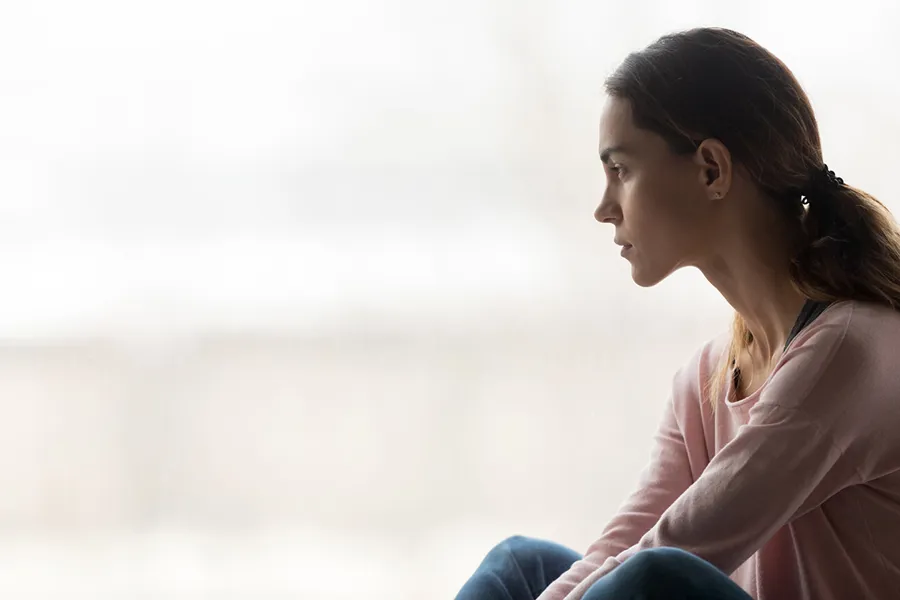 En kvinne som sitter og ser ut av vinduet og er trist