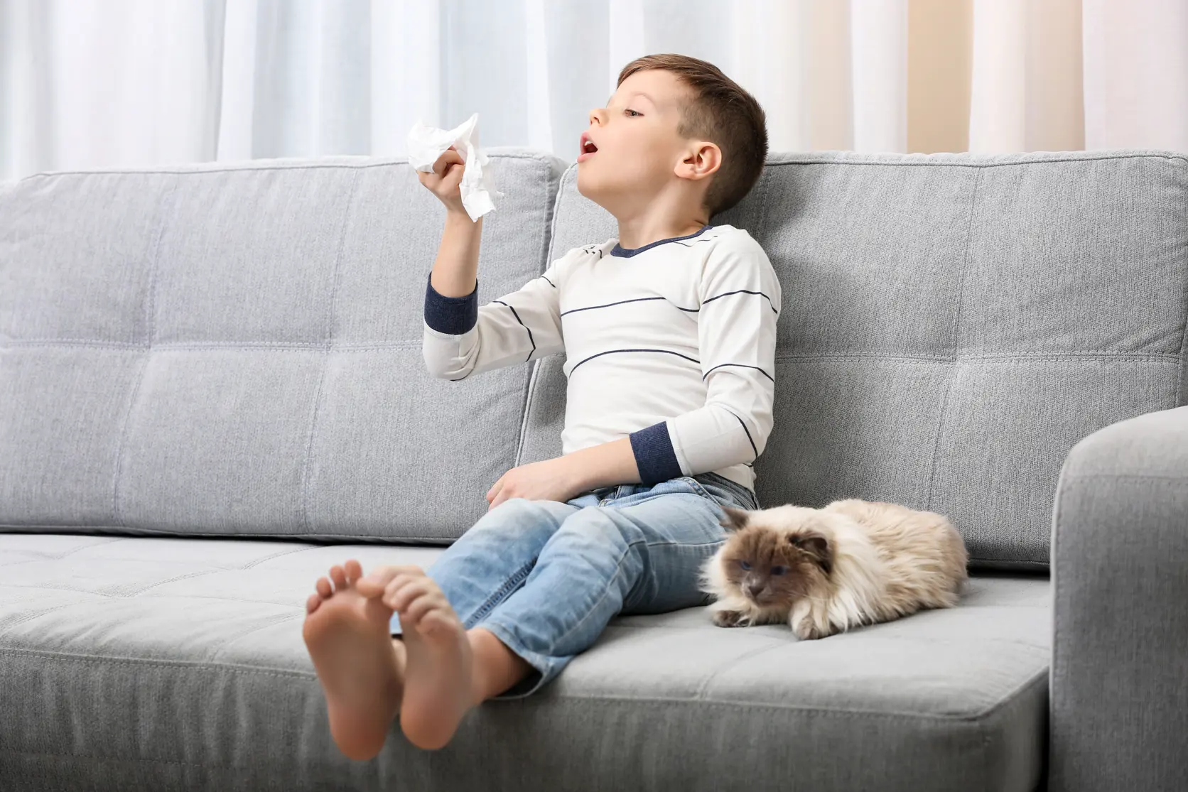 Bilde av en liten gutt som sitter i en sofa med en hund ved siden av seg og nyser