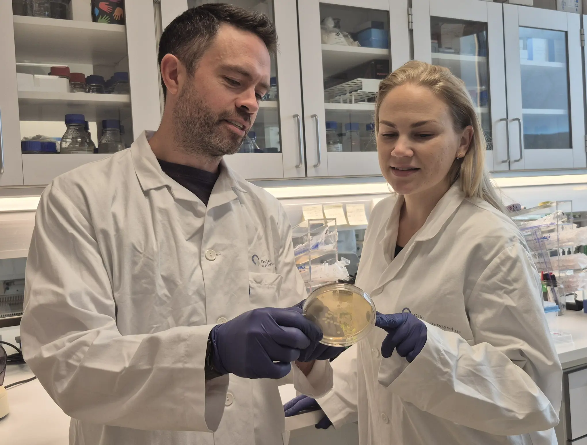 En mann og en kvinne i laboratoriefrakker som ser på et eksemplar