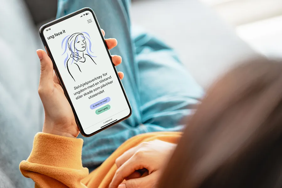 En person som holder en telefon med selvhjelpsvertøyet Ung Face it på skjermen