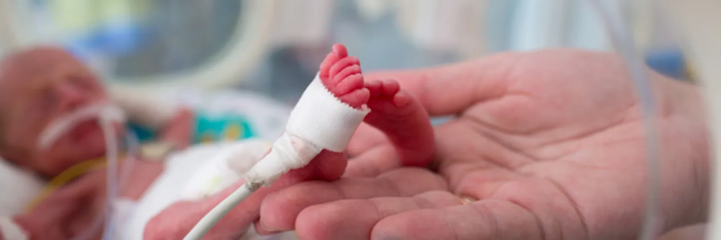 Hender som holder føttene til en prematur baby