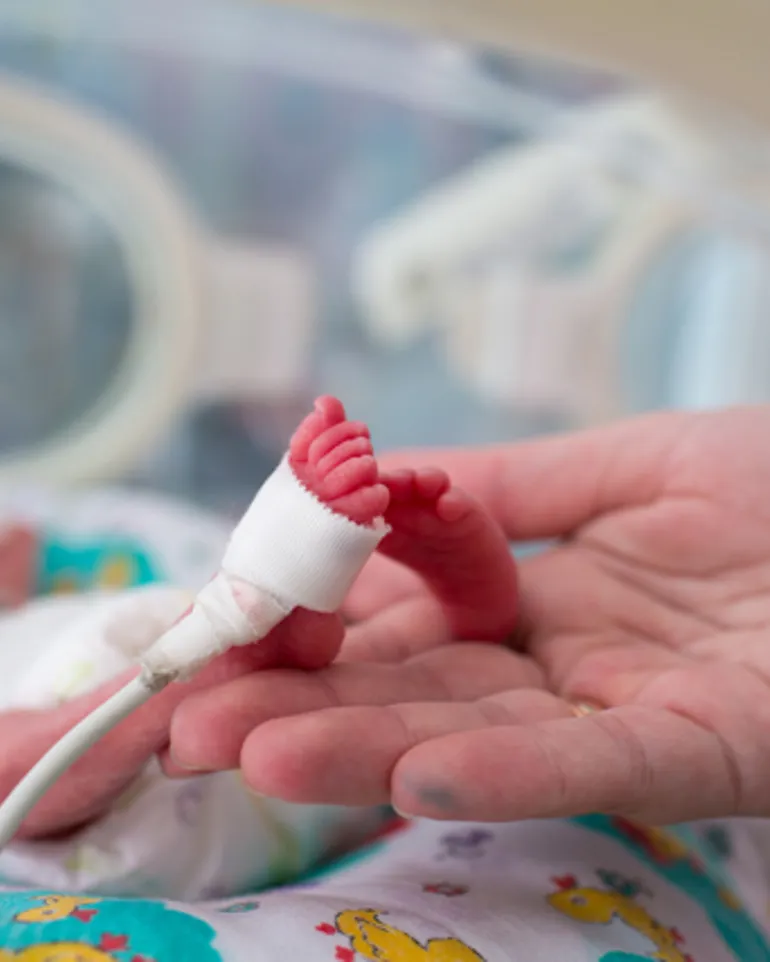 Hender som holder føttene til en prematur baby