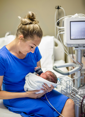 En mor som sitter på en sykeseng og holder sin premature baby
