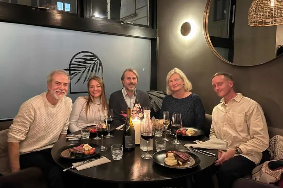 En gruppe mennesker som sitter rundt et bord med mat og drikke