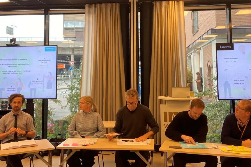 En gruppe mennesker som sitter ved et bord foran en skjerm