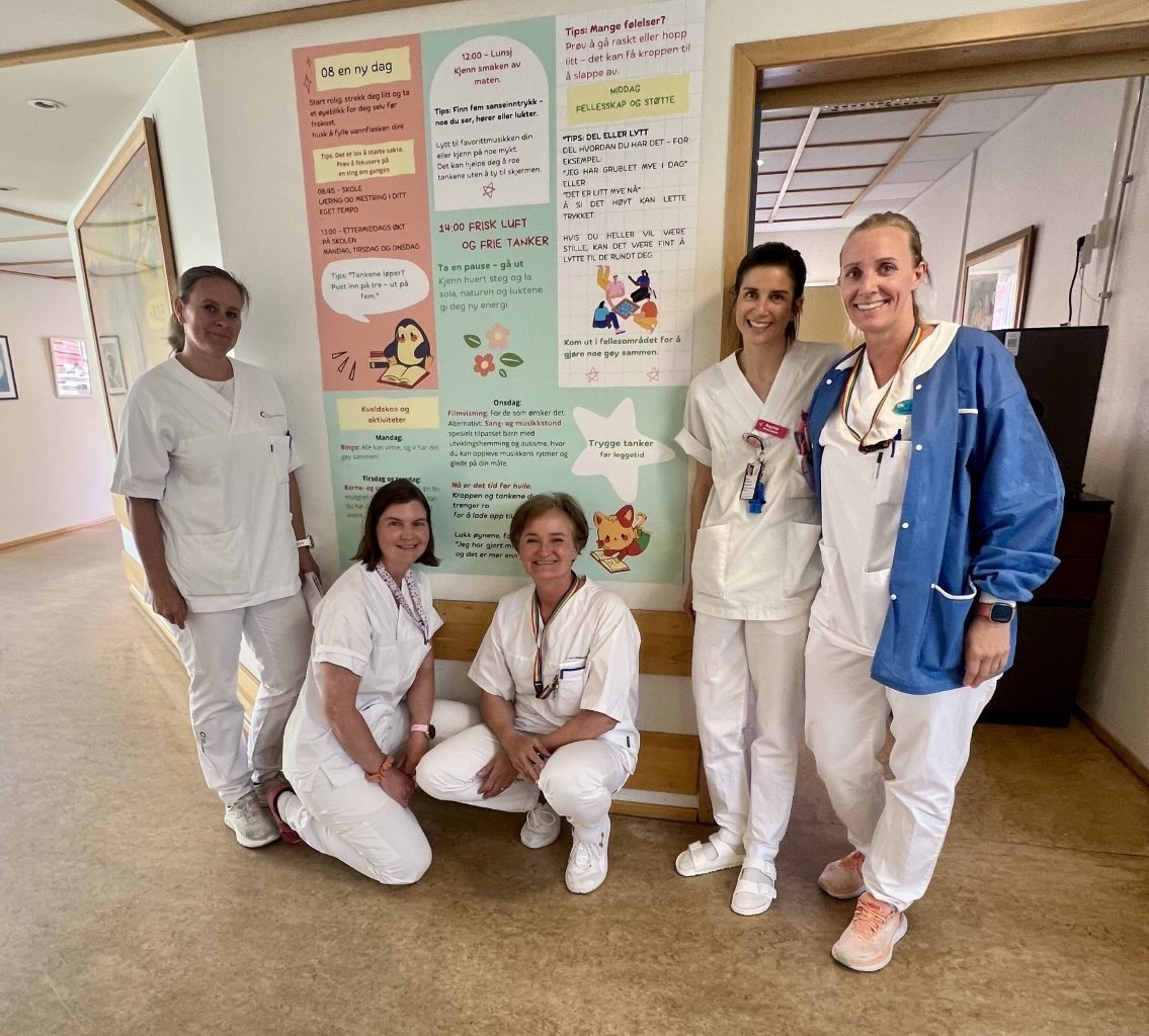 Sykepleiere på sengepost for barn og ungdom på SSE poserer foran en plakat.