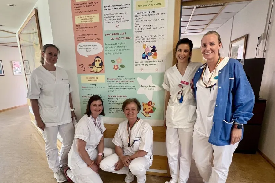 Sykepleiere på sengepost for barn og ungdom på SSE poserer foran en plakat.