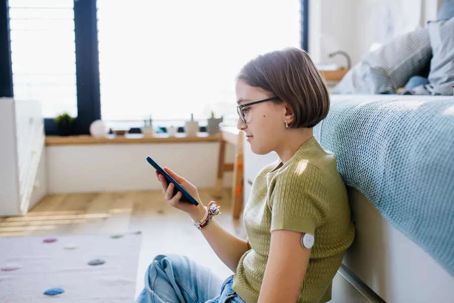 En jente som sitter på gulvet og ser på telefonen sin. Hun har et måleinstrument på armen