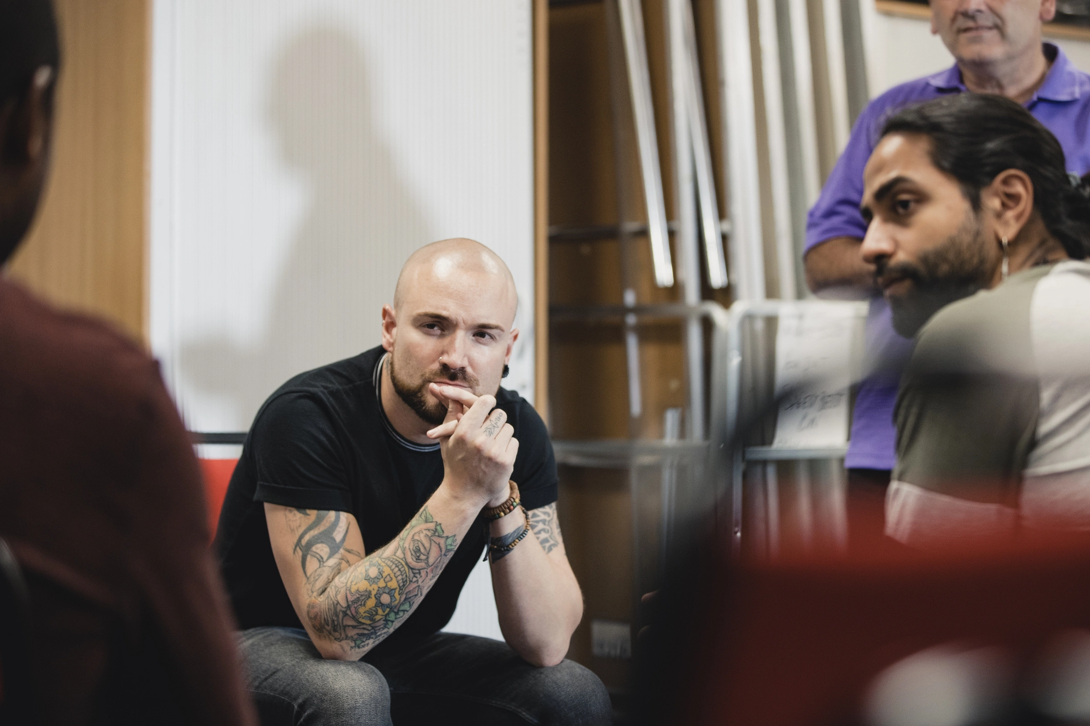 En person med tatoveringer som sitter i en stol sammen med andre menn