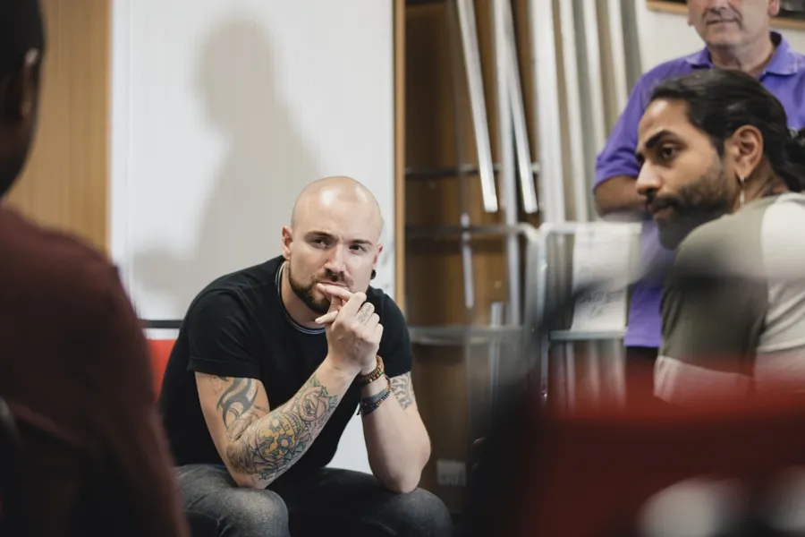En person med tatoveringer som sitter i en stol sammen med andre menn