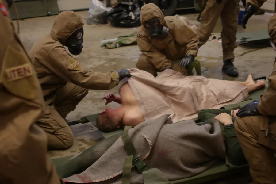 Bilde fra praktisk øvelse i CBRNE-hendelser. En gruppe mennesker i beskyttelsesutstyr som tar seg av en person som ligger på bakken