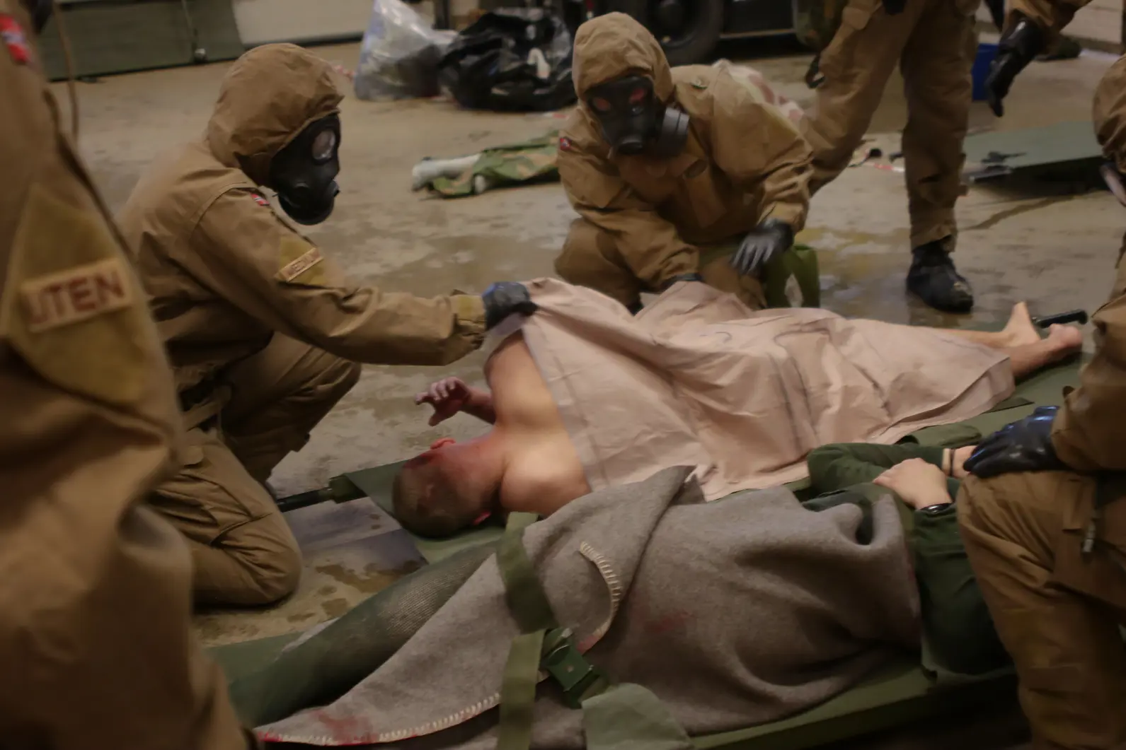 Bilde fra praktisk øvelse i CBRNE-hendelser. En gruppe mennesker i beskyttelsesutstyr som tar seg av en person som ligger på bakken