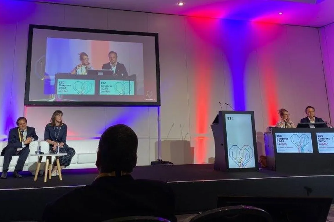 A group of people sitting on a stage with a large screen