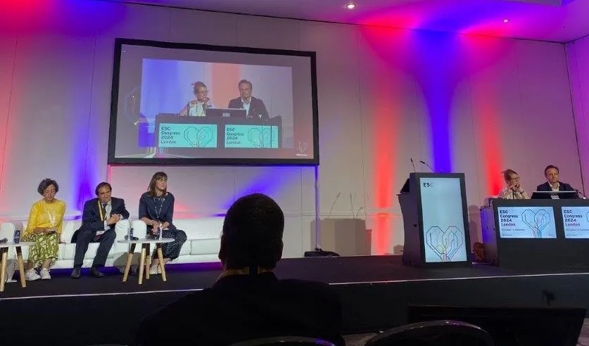 A group of people sitting on a stage with a large screen