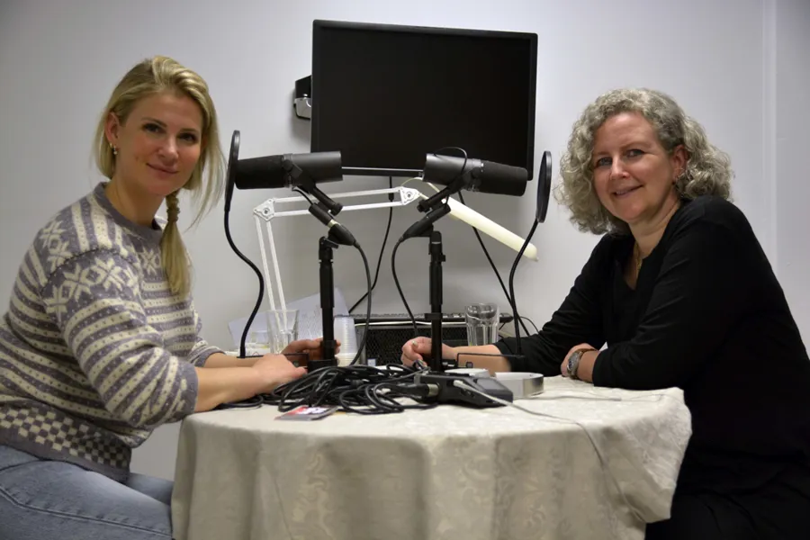 Et par kvinner som sitter ved et bord med datamaskin og mikrofon