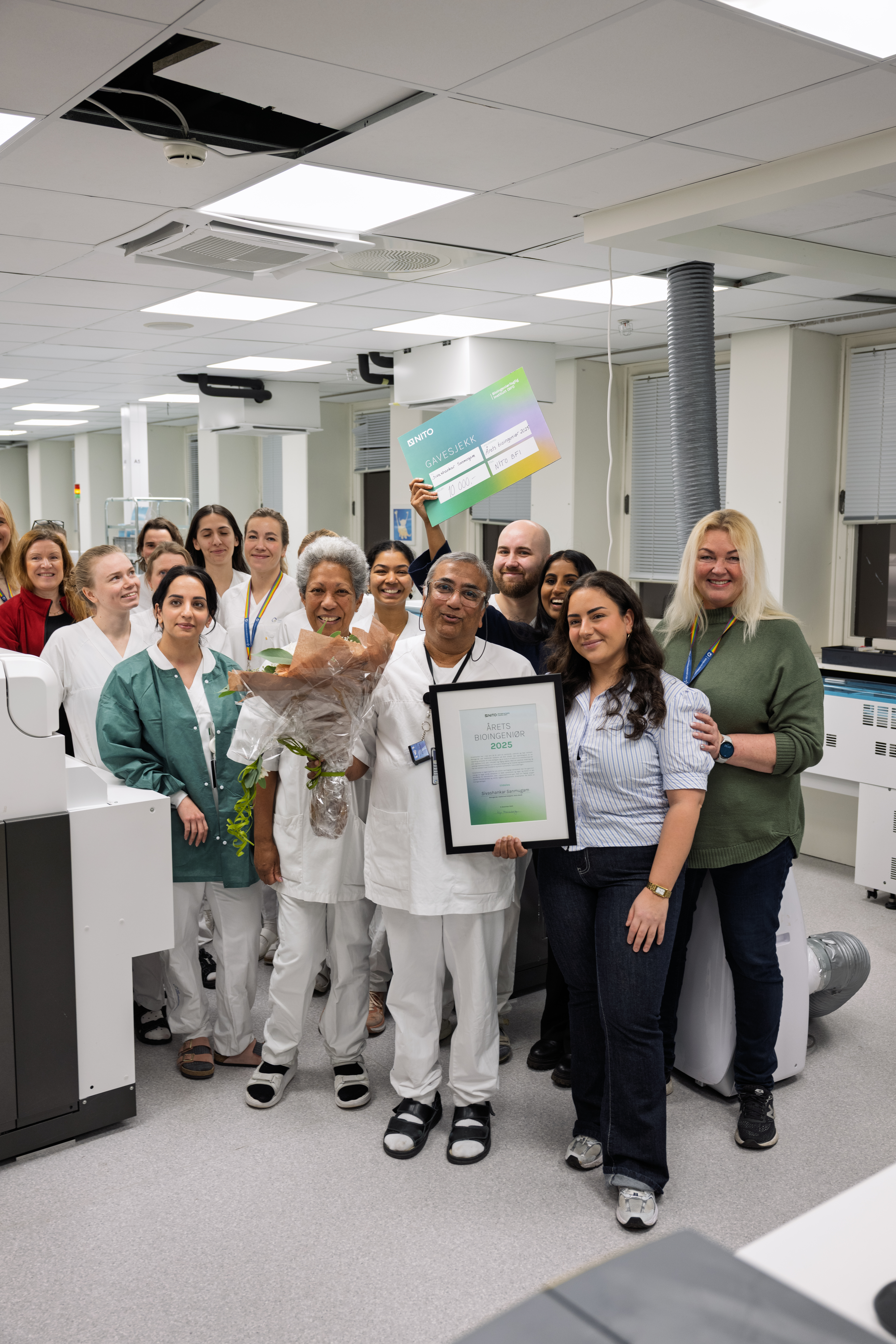 En gruppe mennesker hvor personen i midten holder blomster og en pris