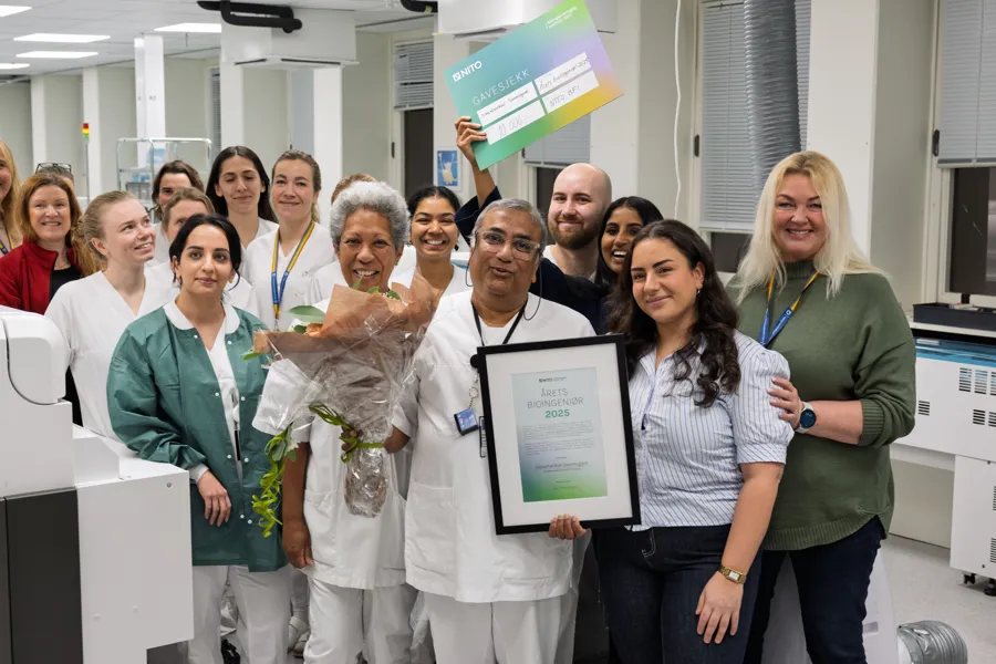 En gruppe mennesker hvor personen i midten holder blomster og en pris