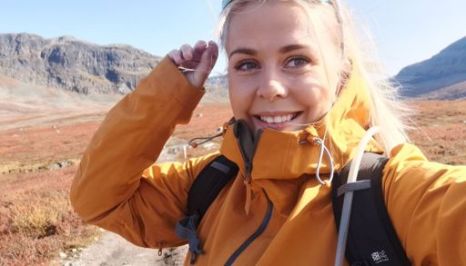 En jente som har på seg en ryggsekk og smiler til kameraet