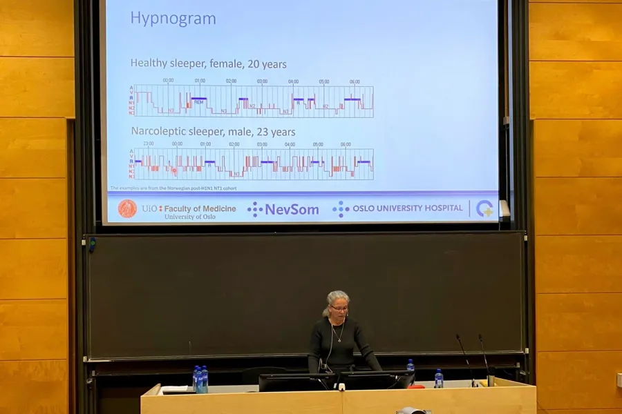 En dame på et podium foran en stor skjerm