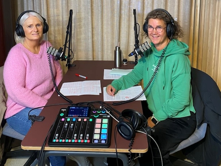 Et par kvinner som sitter ved et bord med platespiller og mikrofoner