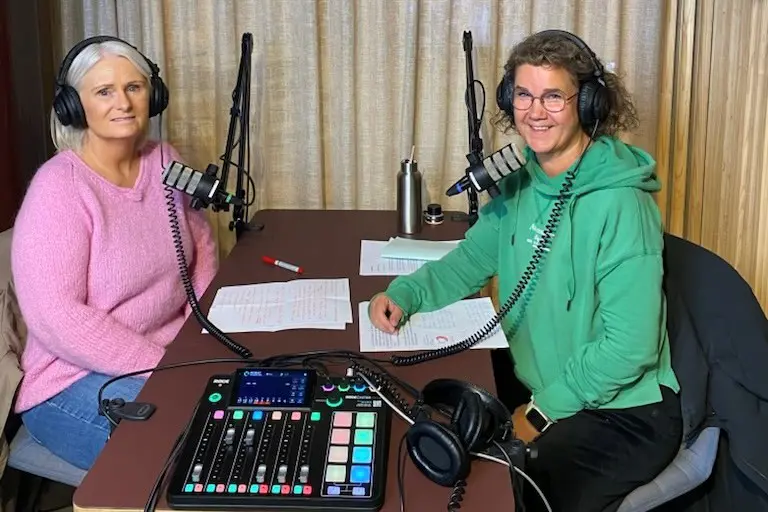 Et par kvinner som sitter ved et bord med platespiller og mikrofoner
