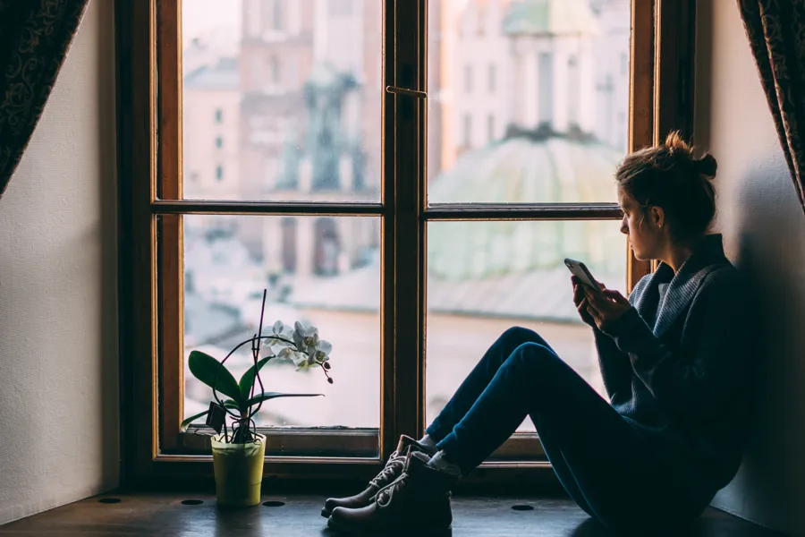 En kvinne som sitter i en vinduskarm og ser på telefonen sin